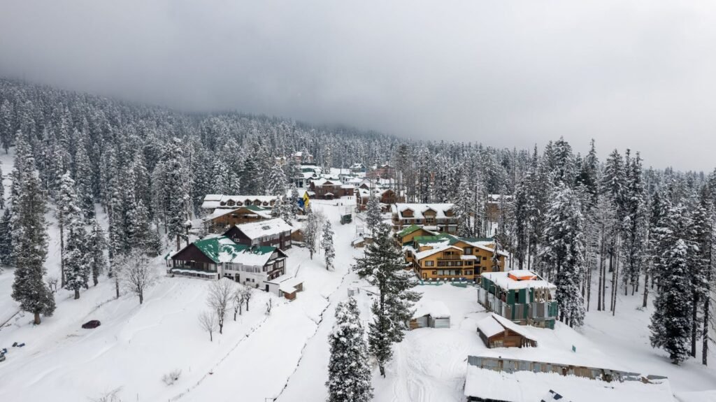 Winter view of Gulmarg, showcasing snow-covered houses and pine trees.