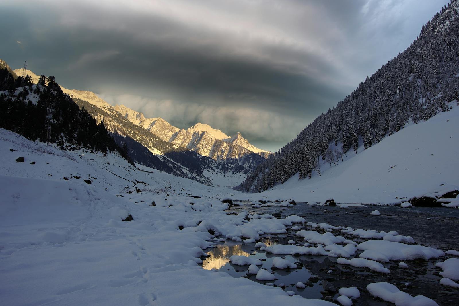 A breathtaking view of snow-covered mountains and serene river in Sonamarg, Kashmir during winter.